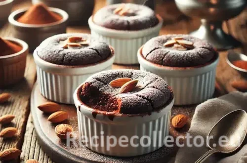 Individual ramekins filled with baked chocolate almond pudding, lightly dusted with powdered sugar, sitting on a rustic wooden surface surrounded by whole almonds and cocoa.